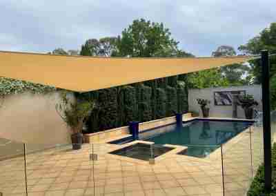 Outdoor picture of a shade sail over a swimming pool and pavers. The property has just been pressure cleaned.