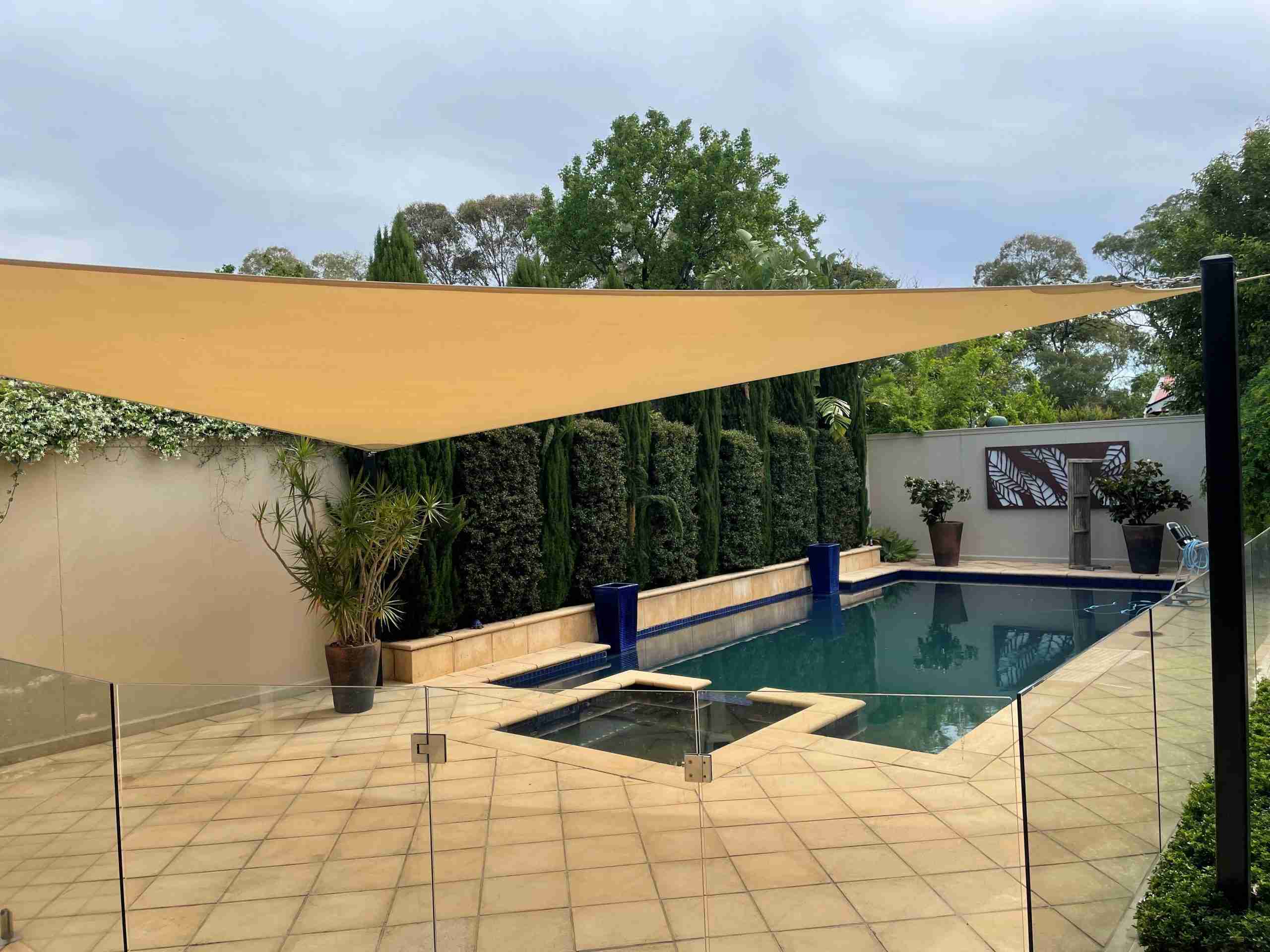 A clean tan shade sail over a paved pool area after residential pressure cleaning