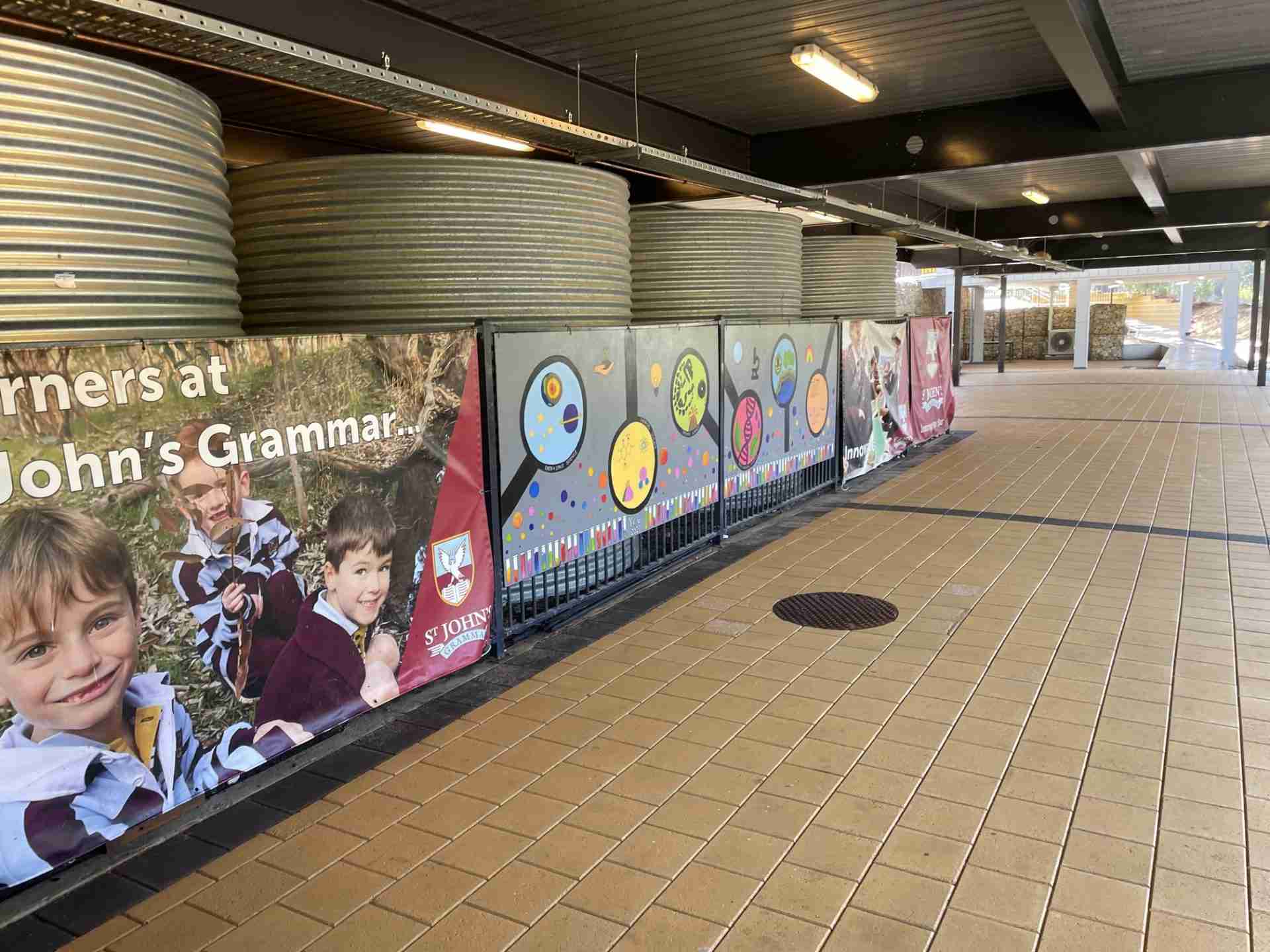 St-Johns-School-Concrete-Clean-after A picture of pavers after a high-pressure clean at St John's Grammar School. Water tanks sit behind a colourful banner and paintings on a fence. In the foreground are clean pavers after a high-pressure clean.