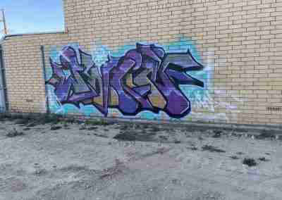 Purple and blue graffiti on a beige brick wall. Adelaide graffiti removal commercial property management
