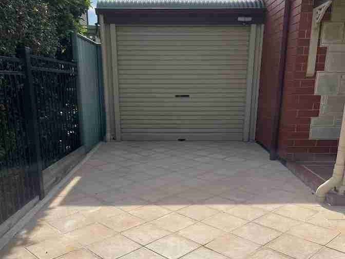 Clean driveway after a pressure-clean. Sand coloured pavers with a sand coloured garage roller door in the background
