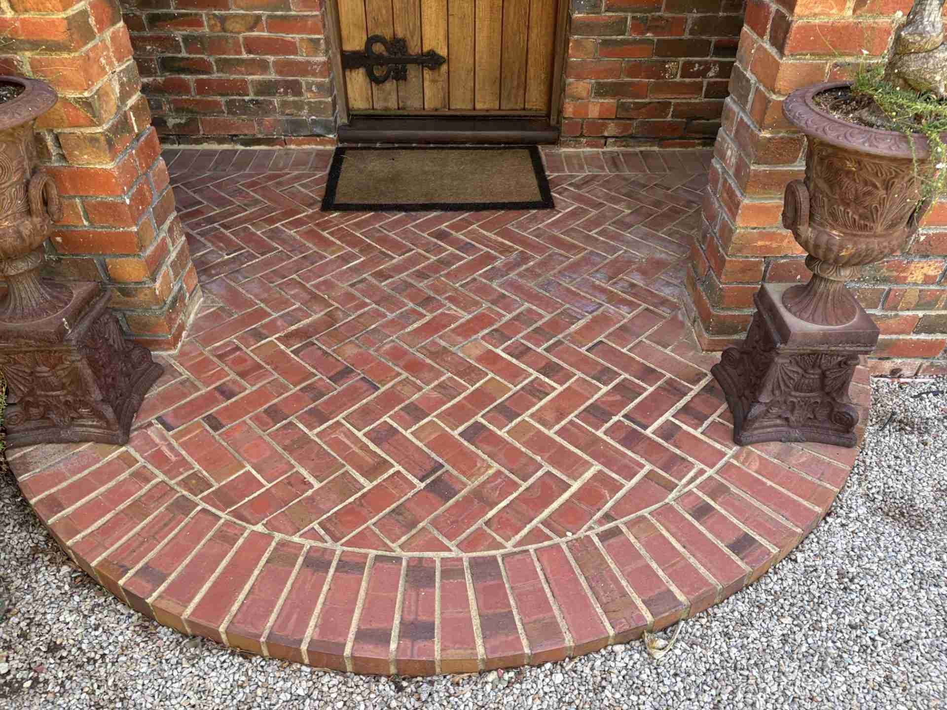 Clean red-brick pavers on a front porch with a door mat in the background
