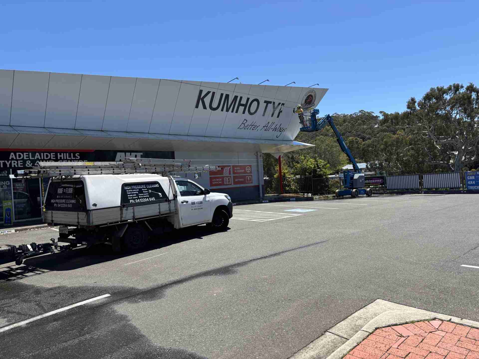 Building-Wash-Mount-Barker-Roof-To-Floor-Maintenance A person pressure washing a building in a cherry-picker, with the Roof to Floor Maintenance work ute parked in front