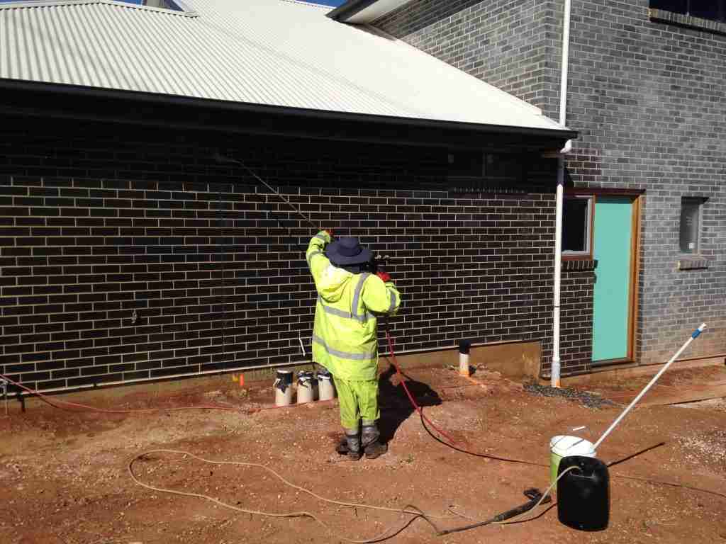 A person in yellow hi visibility clothes performs a brick wash after construction of a house