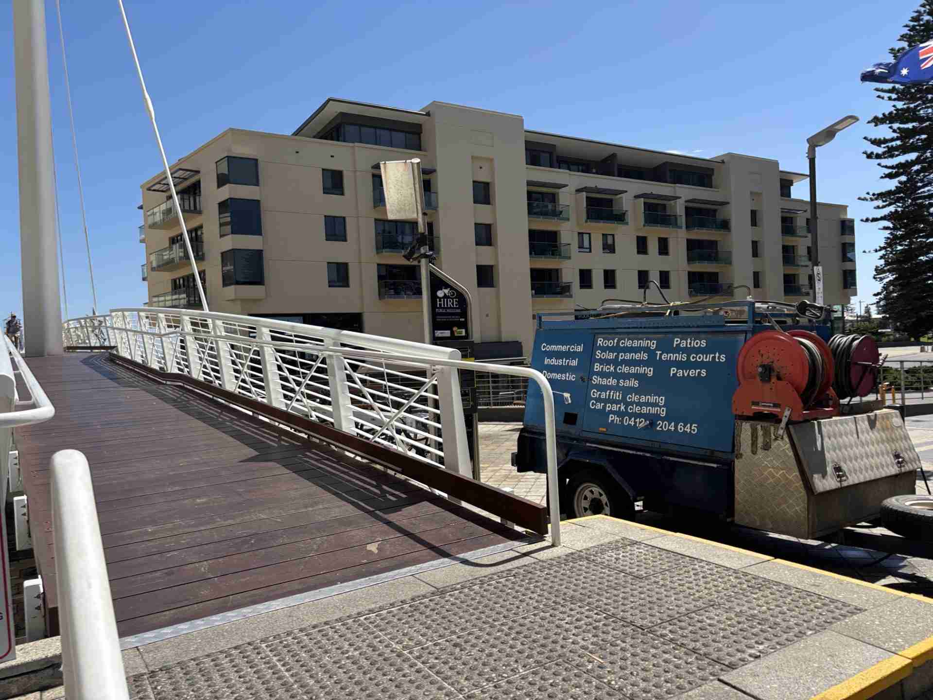 The Roof To Floor Maintenance pressure cleaning company's blue trailer is in the foreground and the Oaks Plaza at Glenelg is in the background.
