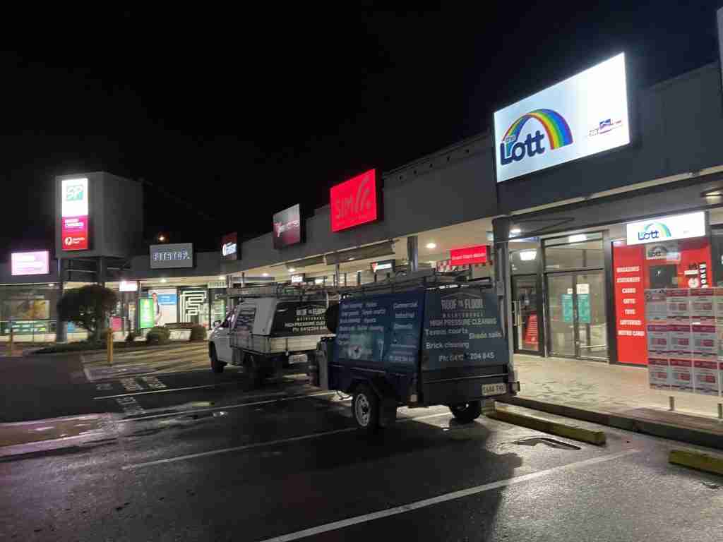 The Roof to Floor Maintenance ute and trailer are parked outside the Southgate Plaza shopping centre at night while conducting a commercial pressure clean
